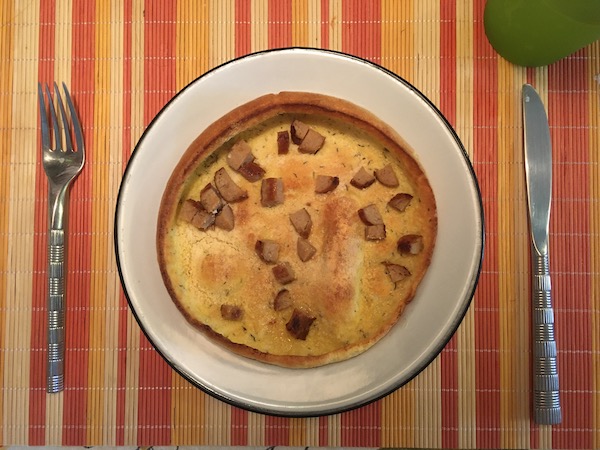 A dutch baby (kind of like a pancake) on a nice plate with a knife and fork