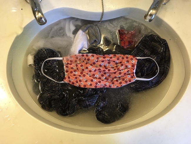 photograph looking down into a sink filled with socks-and-underwear type laundry with a mask on top