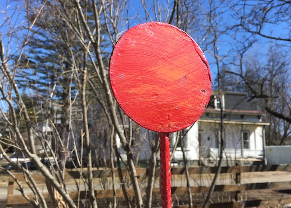 A color photo of a metal disc which is on top of fire hydrants so you can find them in the snow. It's painted a shiny red and is contrasted against the blue of the sky