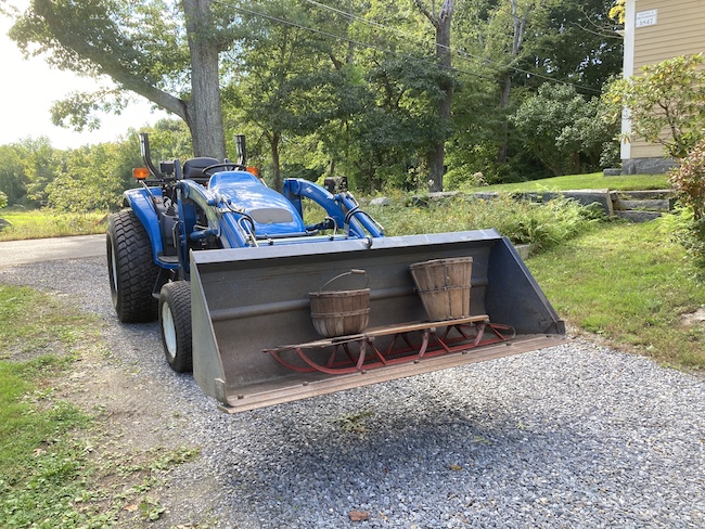 a blue tractor with the bucket holding two apple baskets and a sled