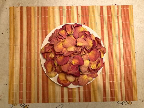 a plate with a bunch of pinkish orange flower petals that rests on an orange and yellow striped placemat