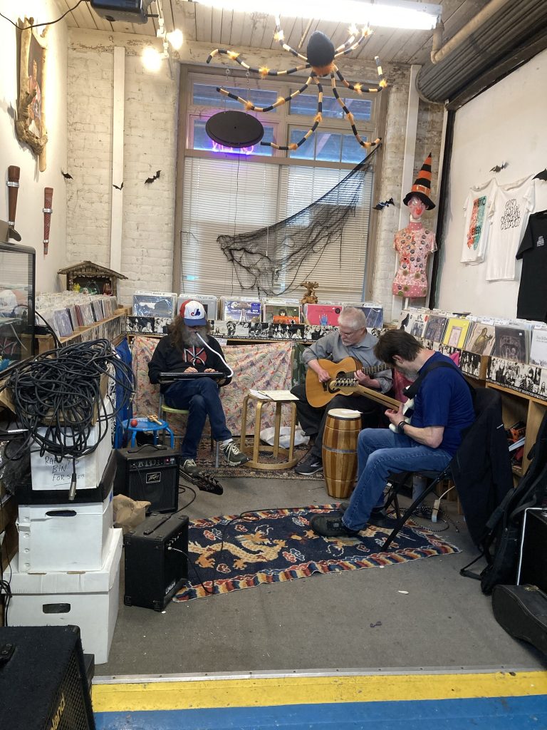 Jim and Todd and Boris playing music at an indie record store. Jim is playing Melodica