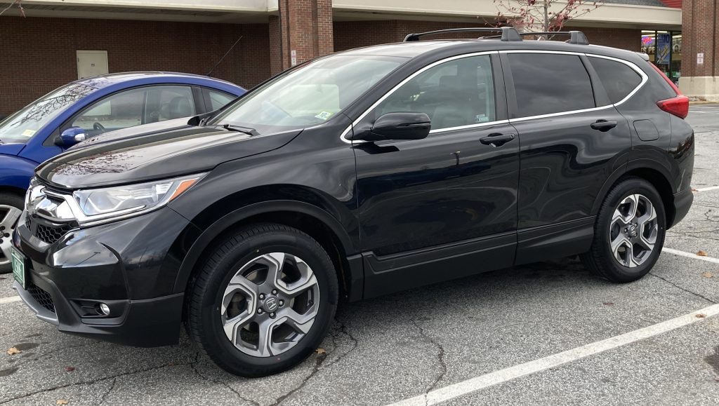 a 20019 Honda CRV in a parking lot. It is black, shiny and has roof racks and dumb flashy hubcaps